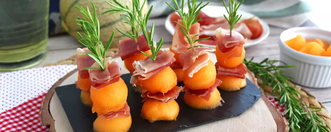 Appetizer skewers with melon, ham, and rosemary
