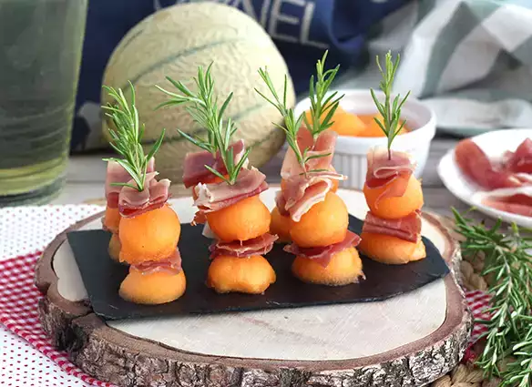 Appetizer skewers with melon, ham, and rosemary